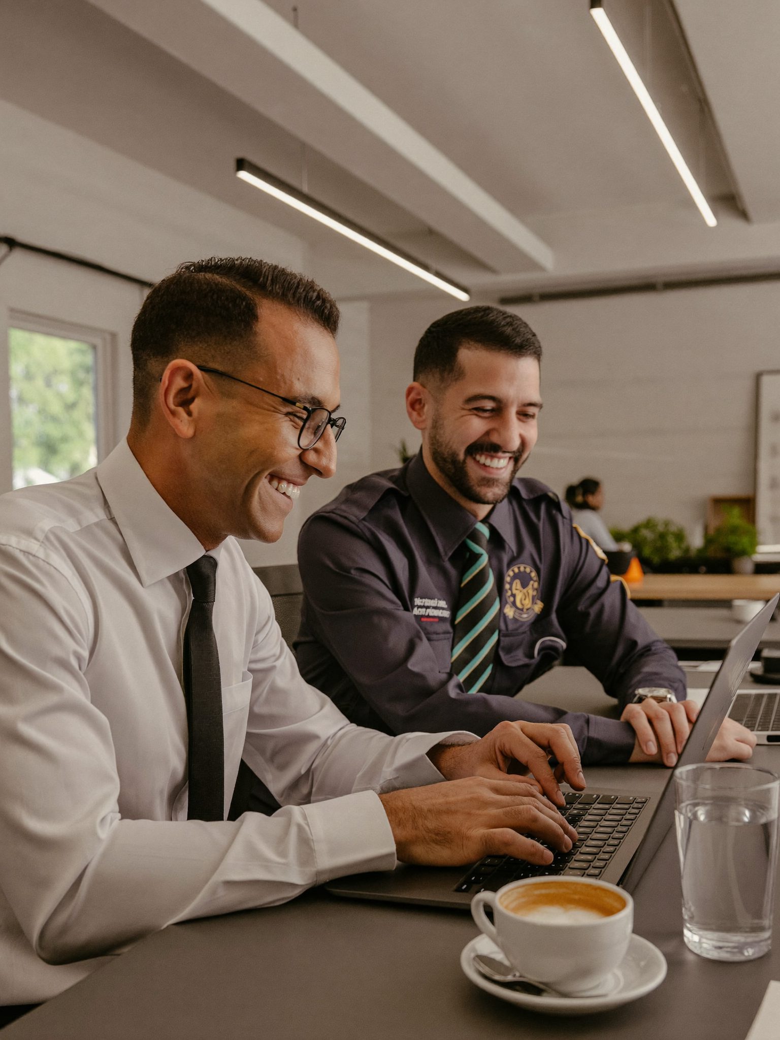 Two reps grinning at one laptop while reviewing a sequence
