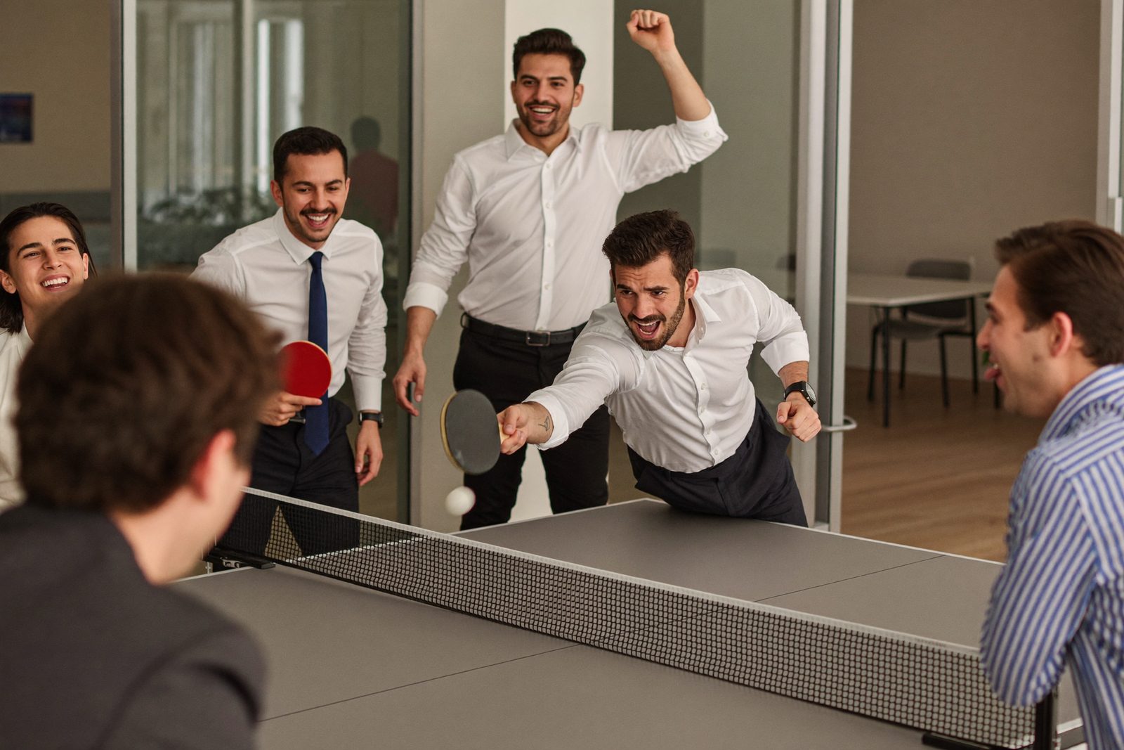 Coworkers diving for a ping-pong ball during a break